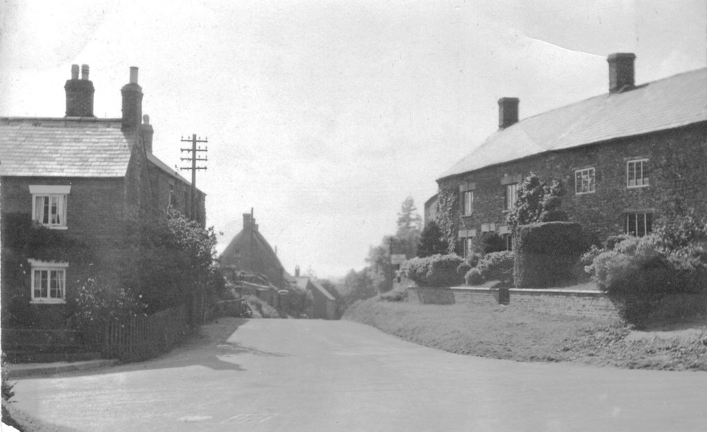 A vintage photo of a dirt road in front of a house